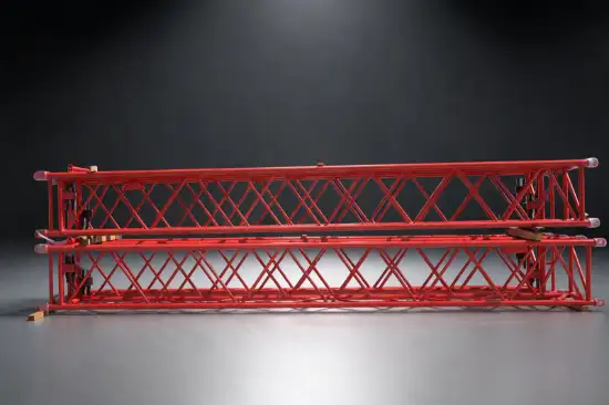 Two red tubular lattice crane jib sections stacked in a workshop display area
