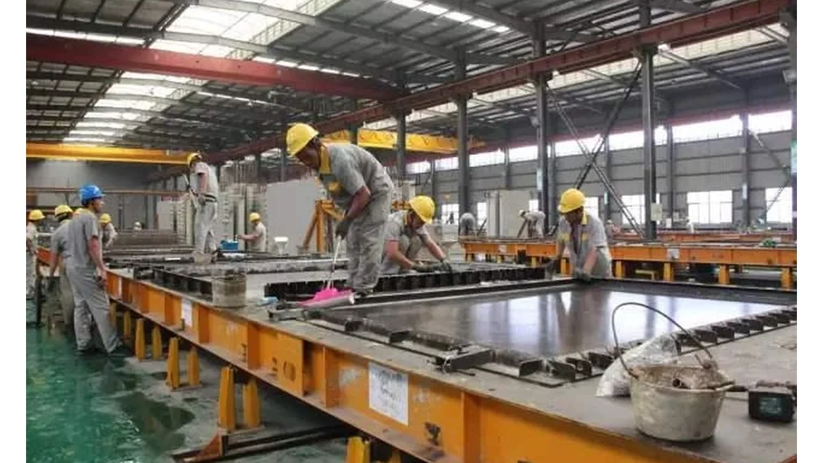 Workers positioning steel side forms on a long casting bed inside a precast concrete plant