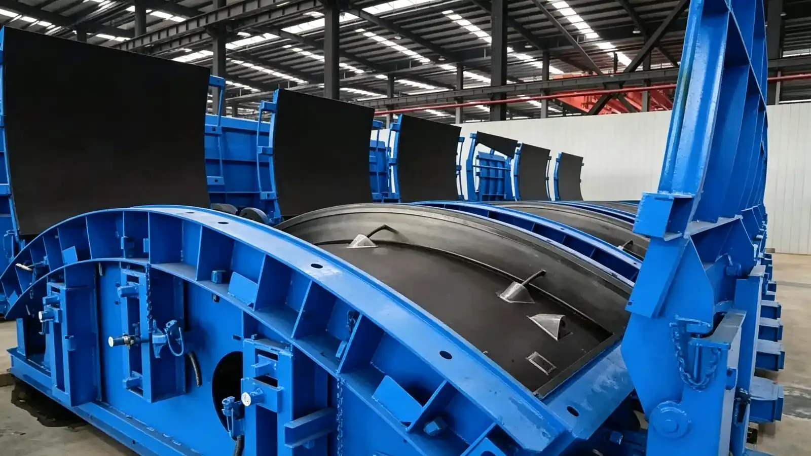 Rows of blue steel moulds with curved contact surfaces for precast tunnel lining segments