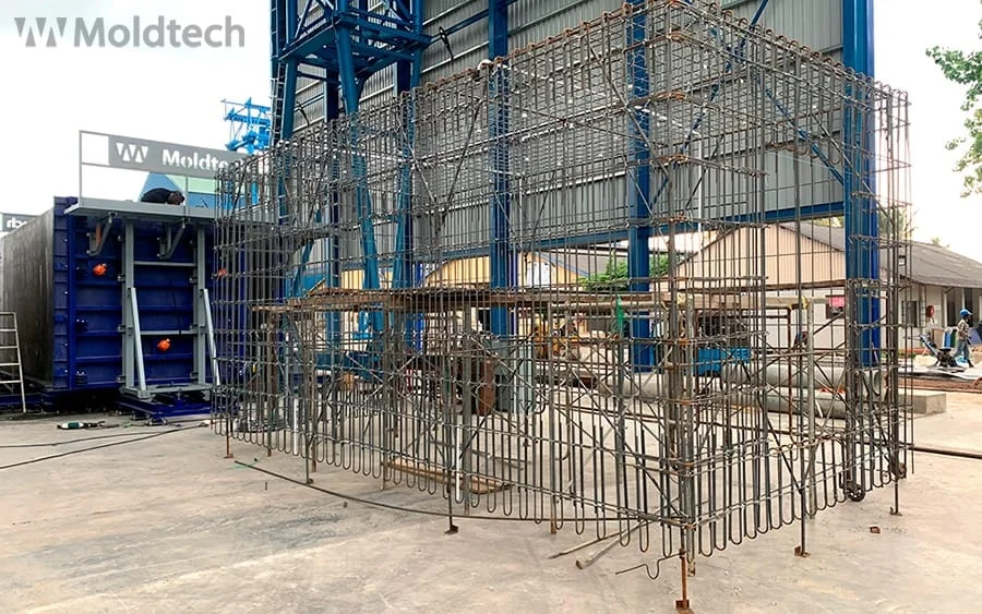 Spatial steel rebar cage suspended beside a PPVC mould at a production facility