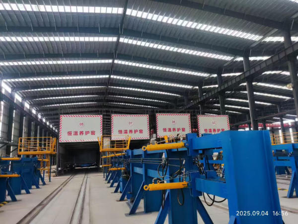 Multiple hydraulic cylinders installed on blue steel formwork beside precast curing chambers